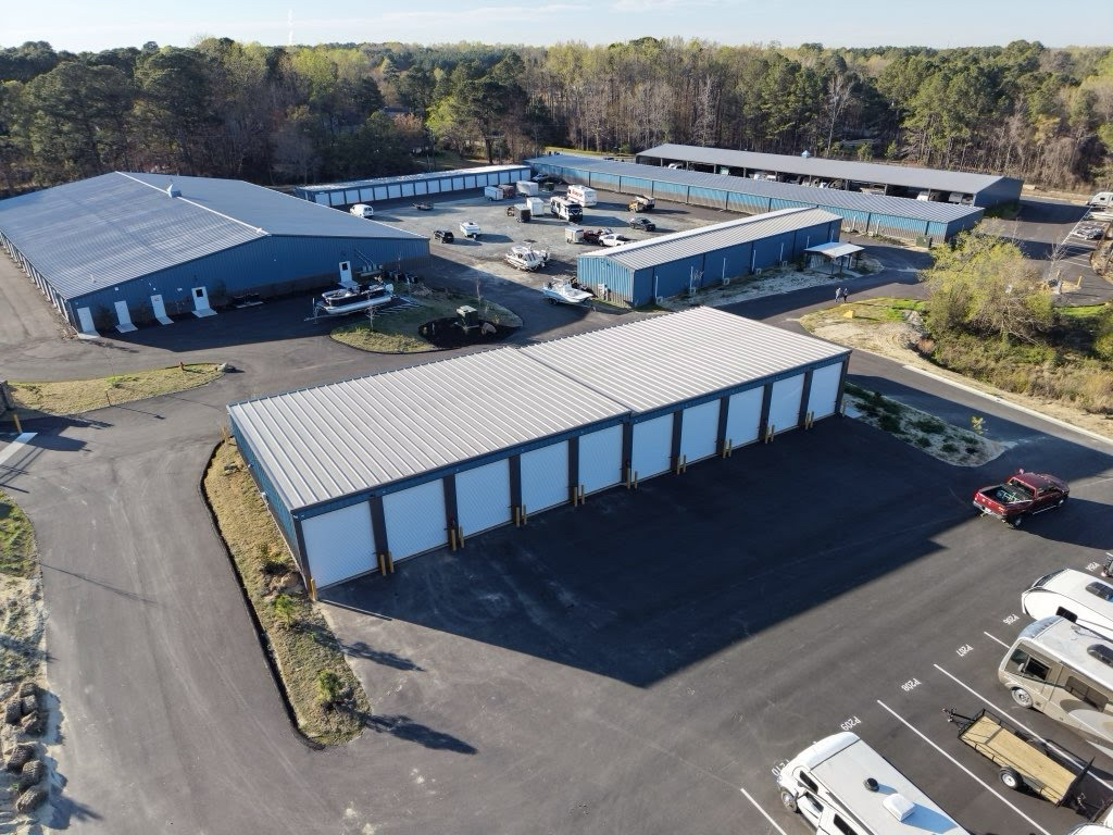 Aerial view of Baucom Business Plaza showing multiple storage buildings, RV parking, and a maroon SUV alongside pines and ponds