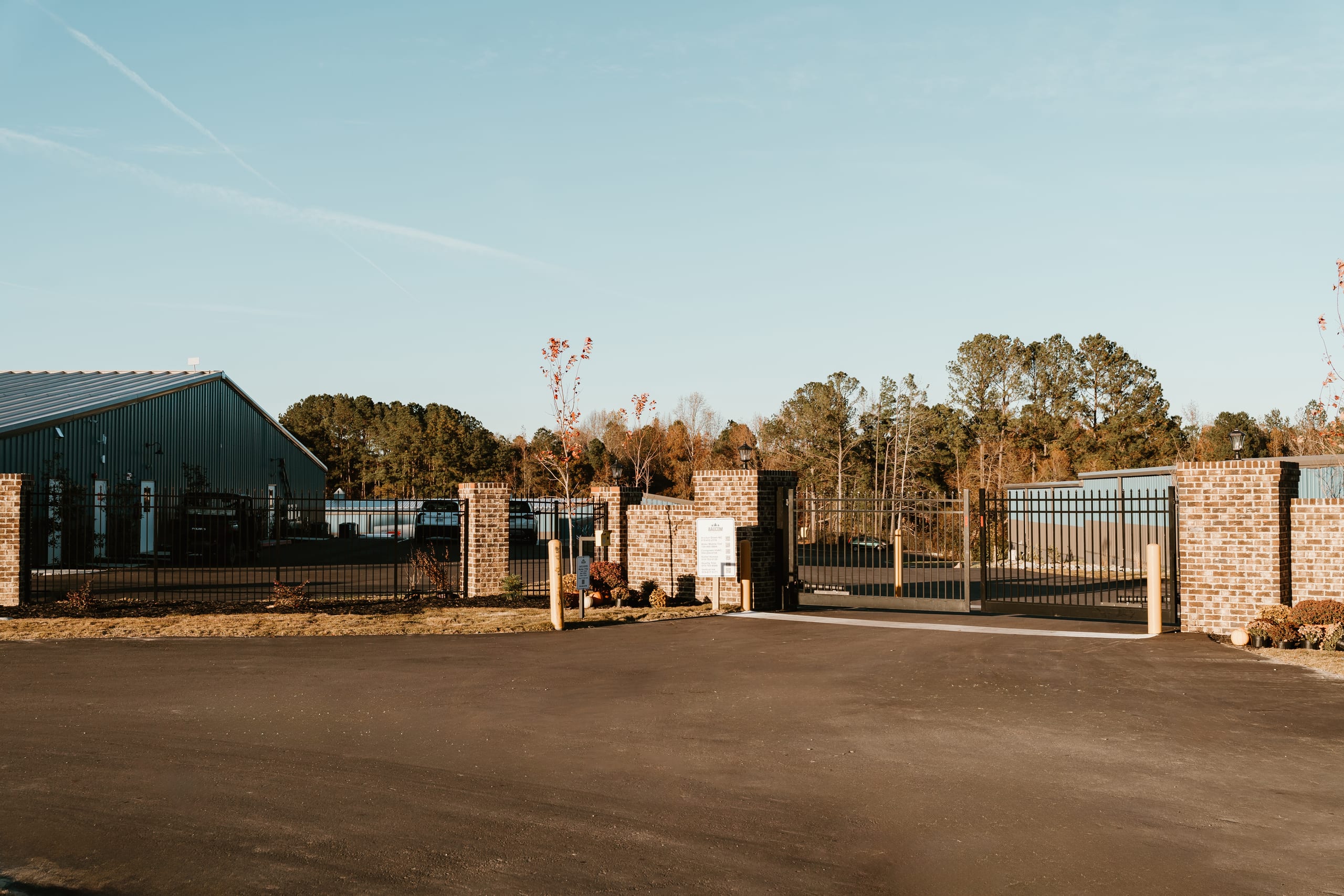 Gated brick entrance to Baucom Business Plaza with masonry pillars, a black metal sliding security gate, and the facility sign