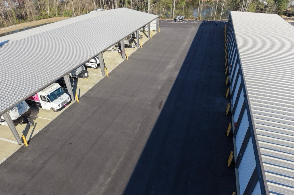 Aerial view of the covered RV and boat canopy parking bay beside a row of drive-up units, with a lake in the background